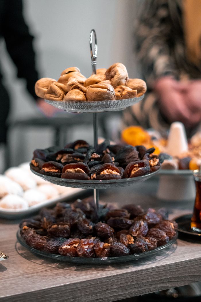 Three-tier dessert stand showcasing figs, dates, and walnuts on a table.